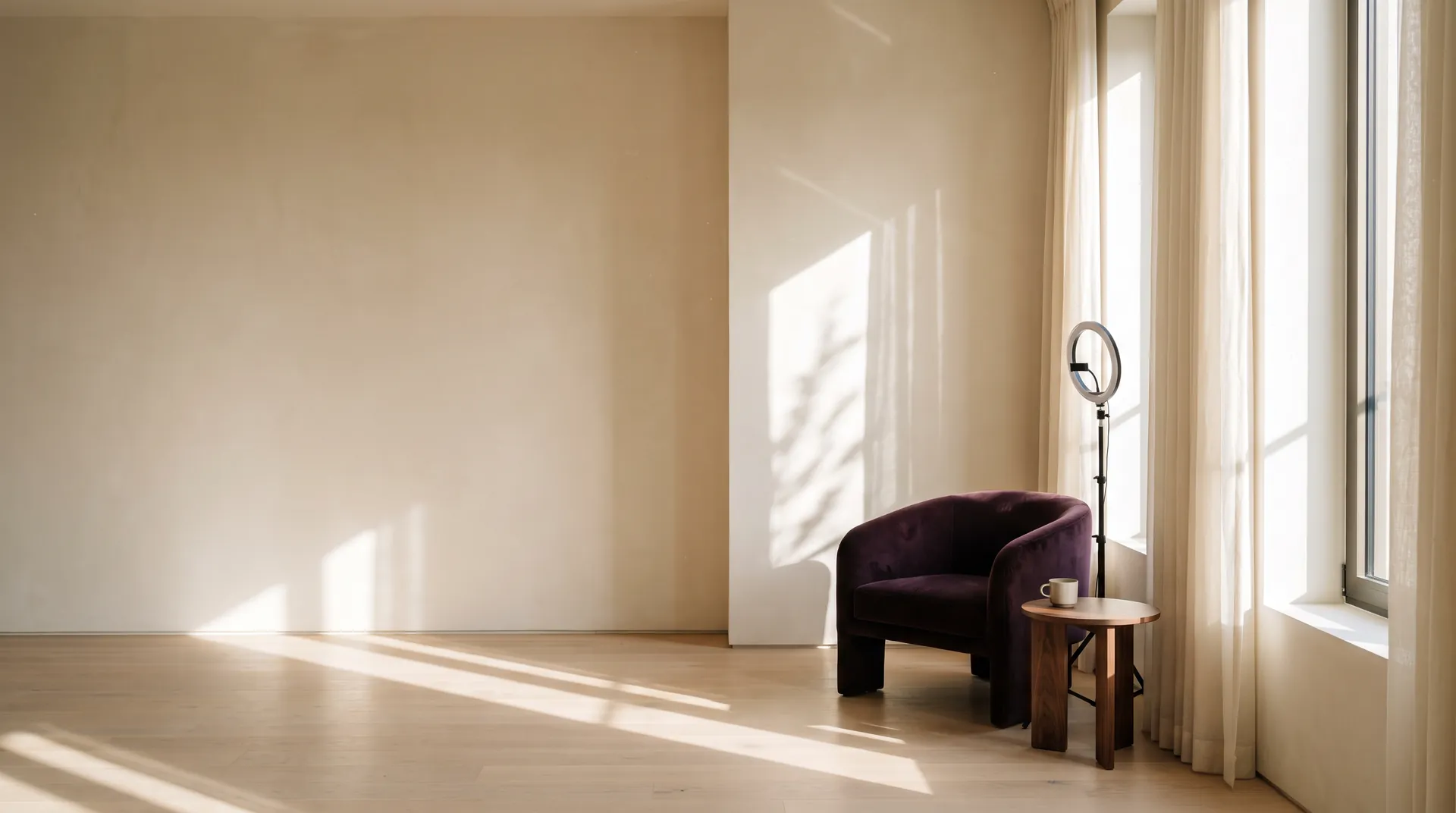 A sunlit creator studio with an empty plum velvet armchair, a walnut side table and a ring light by sheer curtains